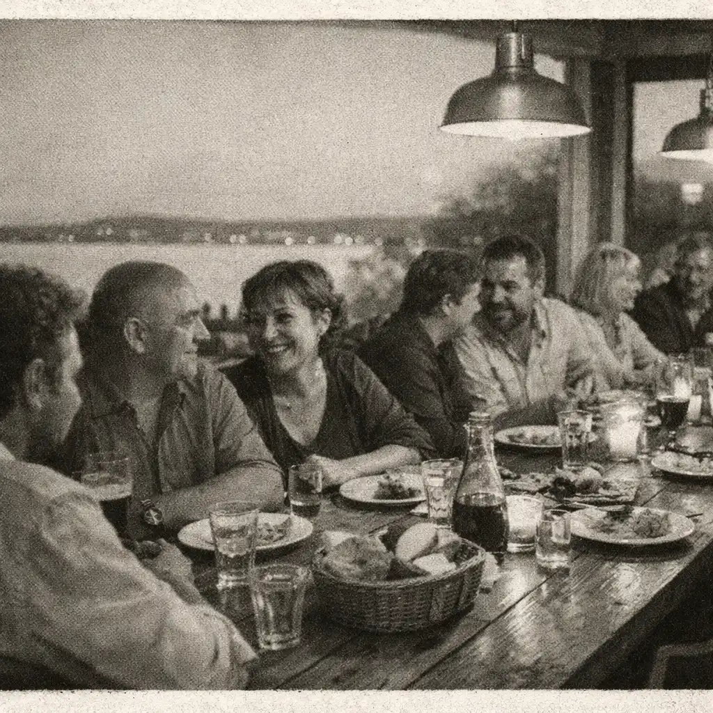 Felnőtt vendégek beszélgetnek és közösen étkeznek egy hosszú éttermi asztalnál.